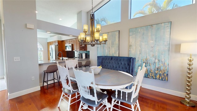 dining room with a high ceiling, a notable chandelier, wood finished floors, and baseboards