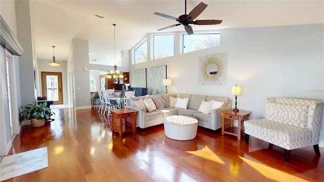 living area featuring visible vents, high vaulted ceiling, ceiling fan with notable chandelier, wood finished floors, and baseboards