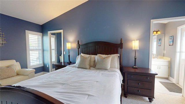 bedroom with baseboards, lofted ceiling, a sink, ensuite bathroom, and light carpet