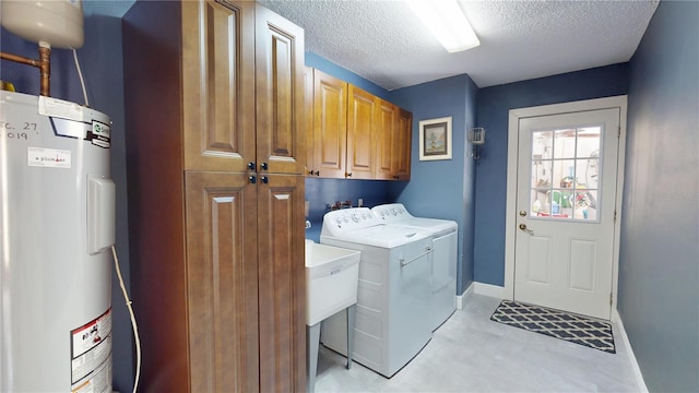 washroom featuring baseboards, washing machine and clothes dryer, cabinet space, a textured ceiling, and electric water heater