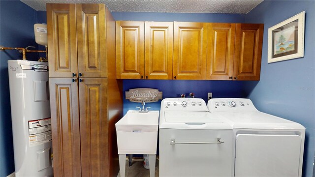 clothes washing area featuring cabinet space, water heater, a sink, a textured ceiling, and washer and clothes dryer