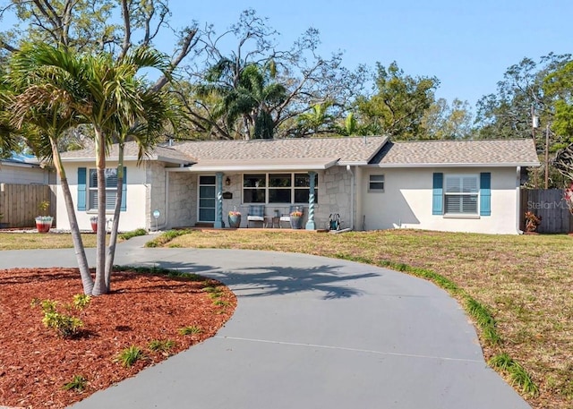 ranch-style house featuring fence, stucco siding, a front lawn, concrete driveway, and stone siding