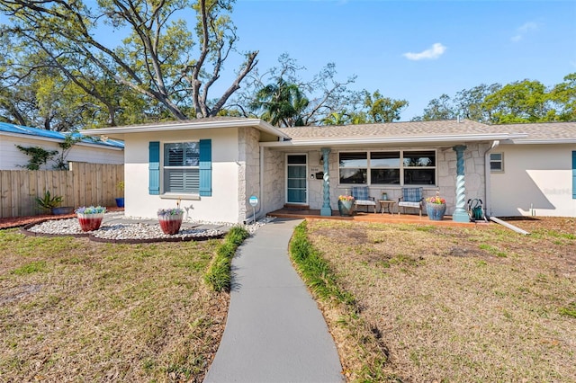 ranch-style house with fence, a porch, a front yard, stucco siding, and stone siding