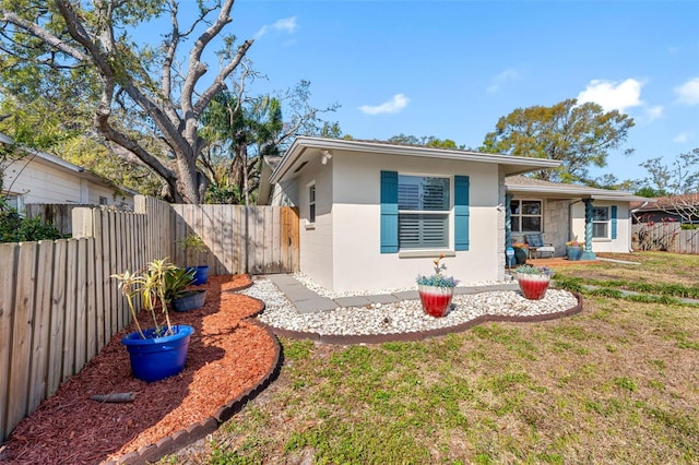 view of front of home with stucco siding, a front yard, and a fenced backyard