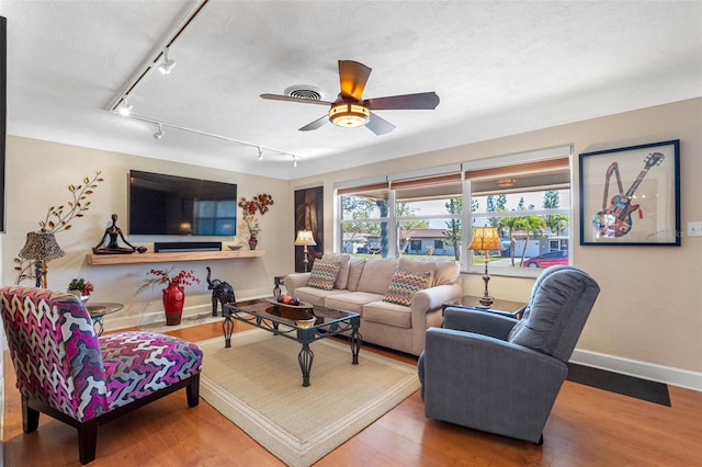 living room featuring visible vents, a ceiling fan, baseboards, and wood finished floors