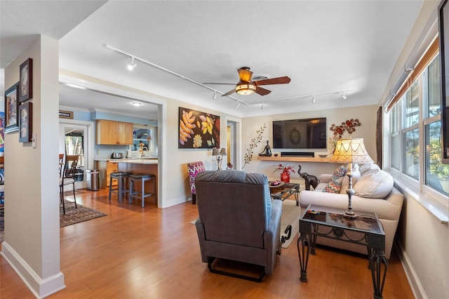 living area featuring rail lighting, baseboards, light wood finished floors, and ceiling fan