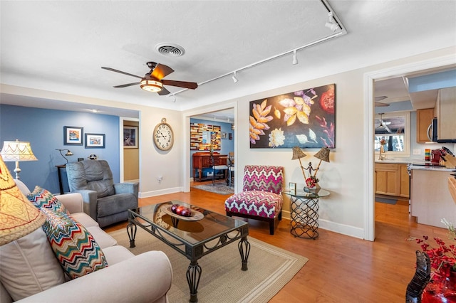 living area with visible vents, light wood-style floors, rail lighting, baseboards, and ceiling fan