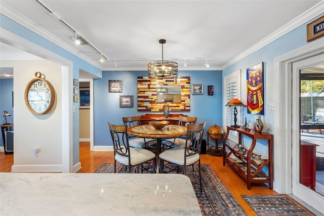 dining space featuring track lighting, wood finished floors, and crown molding