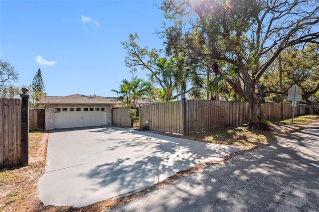 exterior space featuring a garage, stone siding, driveway, and fence