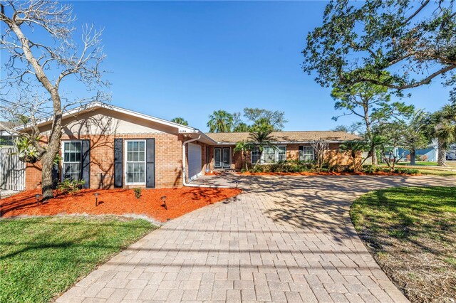 ranch-style house featuring decorative driveway, brick siding, a garage, and a front yard