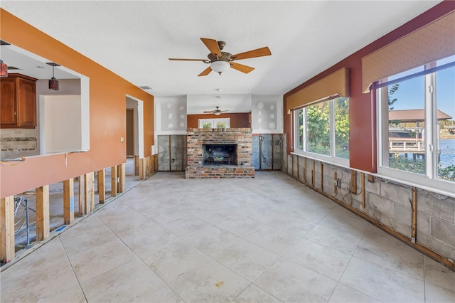 unfurnished living room with visible vents, a textured ceiling, a fireplace, light tile patterned floors, and ceiling fan