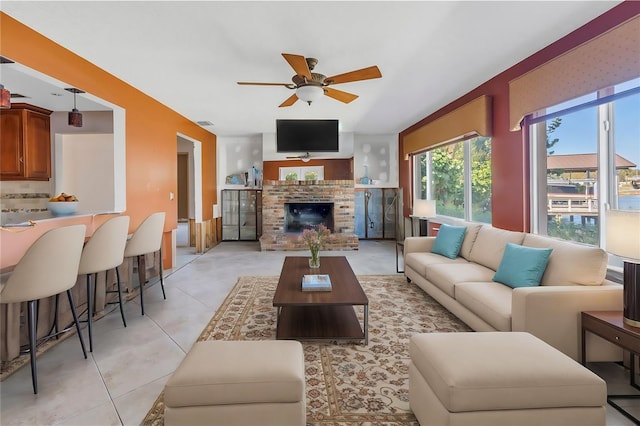 living area with a brick fireplace, light tile patterned flooring, and ceiling fan