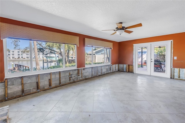 unfurnished room with a ceiling fan, a healthy amount of sunlight, french doors, and a textured ceiling