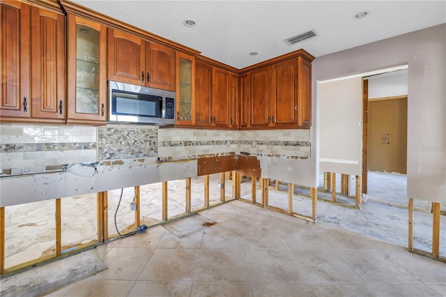 kitchen featuring stainless steel microwave, glass insert cabinets, backsplash, and visible vents