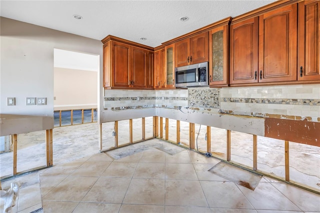 kitchen with stainless steel microwave, light tile patterned flooring, glass insert cabinets, and backsplash