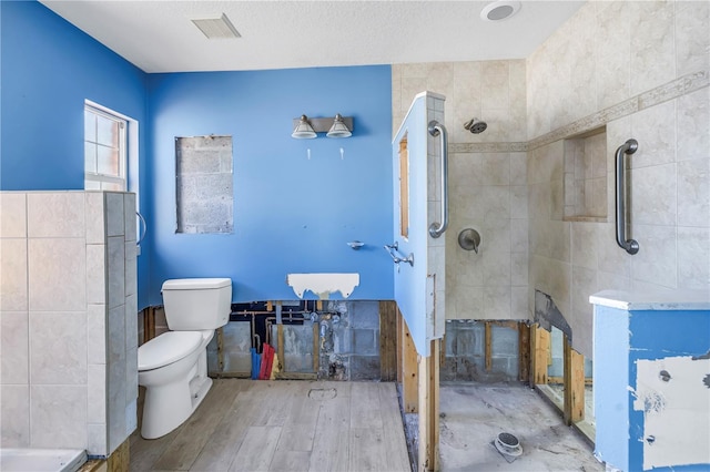 full bath featuring visible vents, toilet, wood finished floors, and tiled shower