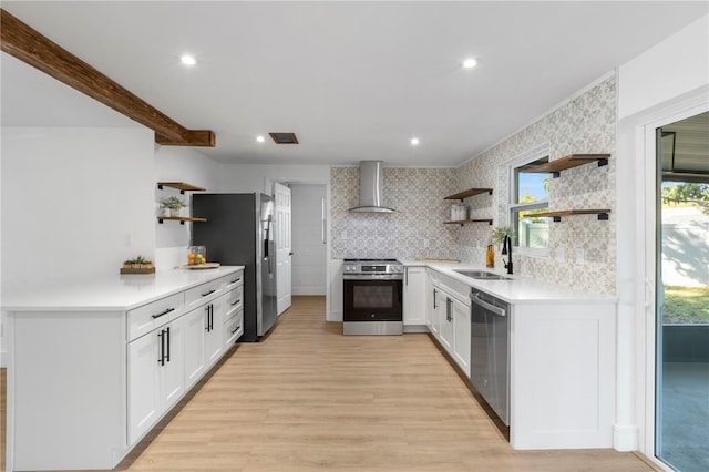 kitchen featuring open shelves, a sink, wall chimney range hood, appliances with stainless steel finishes, and light countertops