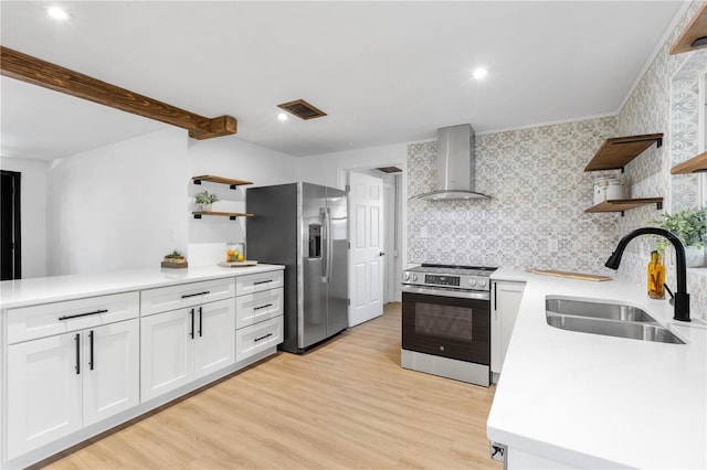 kitchen featuring open shelves, a sink, stainless steel appliances, light wood-style floors, and wall chimney exhaust hood