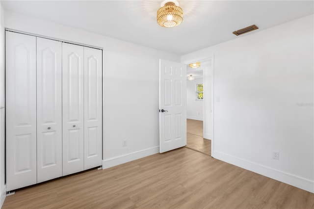 unfurnished bedroom with light wood-style flooring, baseboards, visible vents, and a closet