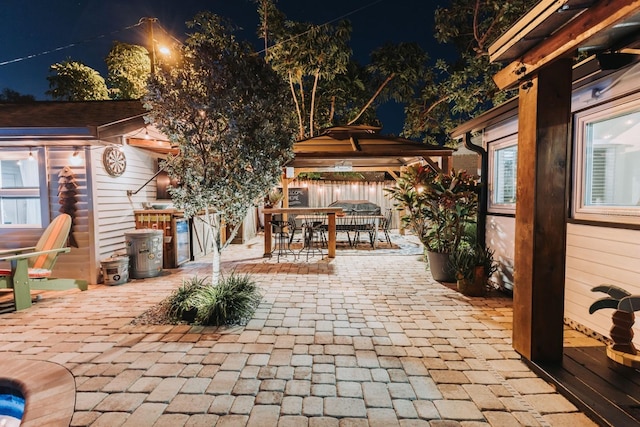 patio at night featuring a gazebo, outdoor dining area, an outbuilding, and fence