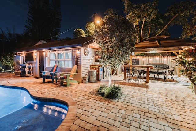 back of house at twilight featuring fence, an outdoor pool, an outdoor structure, a storage structure, and a patio area