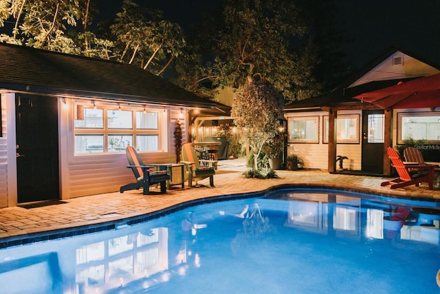 pool at night featuring a patio area, area for grilling, and an outdoor pool