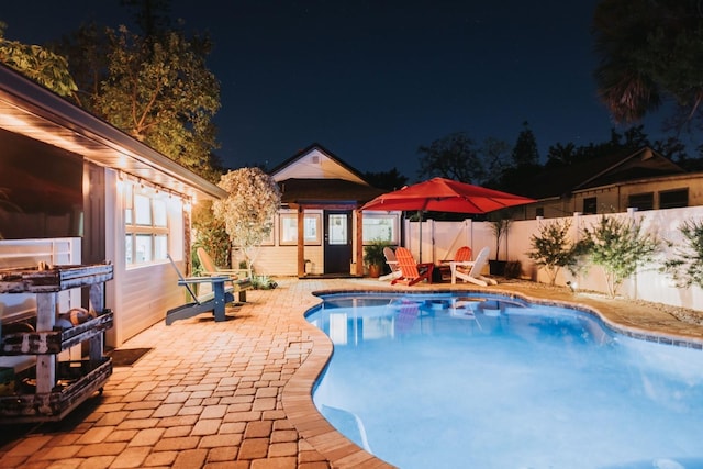 pool at night with a fenced in pool, a fenced backyard, and a patio area