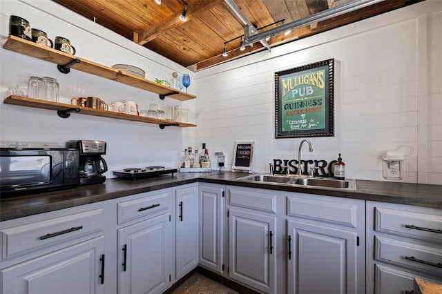 kitchen featuring dark countertops, open shelves, wooden ceiling, and a sink