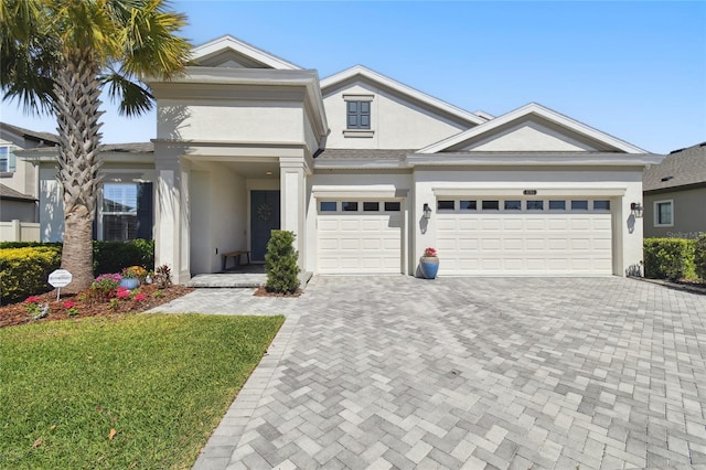 view of front of house featuring stucco siding, decorative driveway, a front lawn, and an attached garage