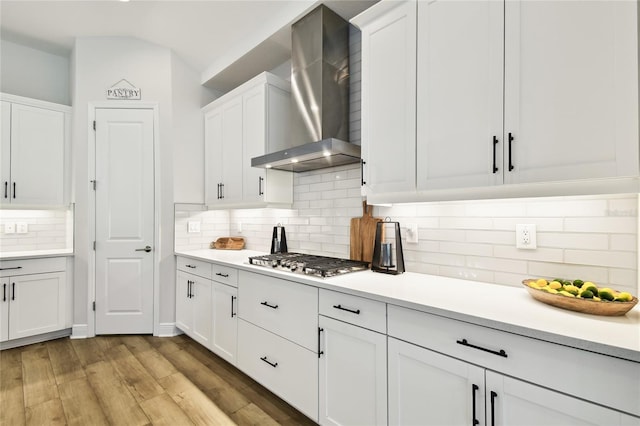 8766 Shadyside Ln, Land O Lakes, FL 34637 - kitchen with wall chimney range hood, stainless steel gas cooktop, white cabinetry, light countertops, and decorative backsplash
