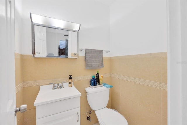 half bathroom with a wainscoted wall, toilet, tile walls, and vanity