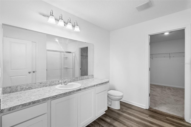 full bathroom featuring visible vents, toilet, wood finished floors, a shower stall, and a spacious closet