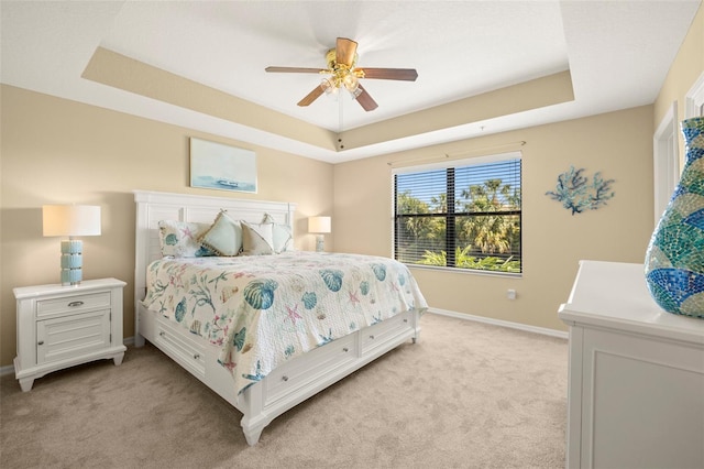 bedroom featuring ceiling fan, a raised ceiling, baseboards, and light carpet