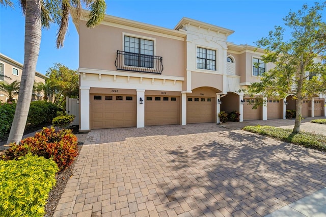 view of front of home featuring a balcony, stucco siding, decorative driveway, and a garage