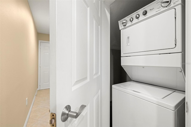 laundry area featuring light tile patterned flooring, laundry area, stacked washer and clothes dryer, and baseboards