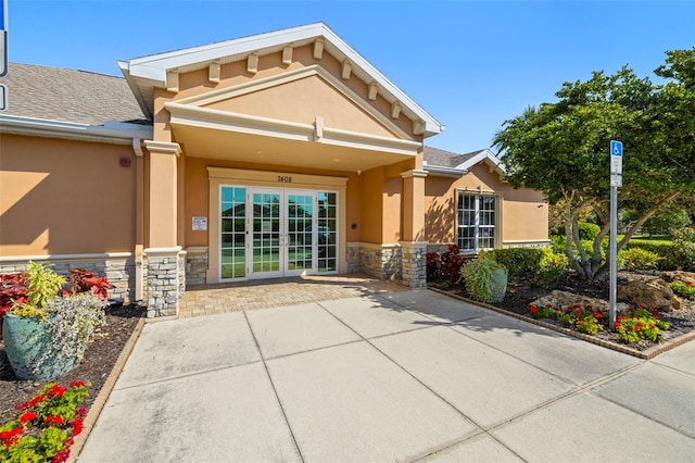 rear view of property featuring a shingled roof, french doors, stone siding, and stucco siding