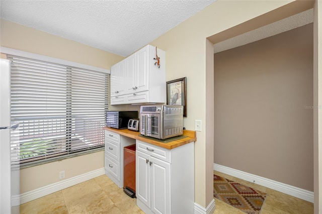 kitchen featuring baseboards, wooden counters, a textured ceiling, and white cabinets