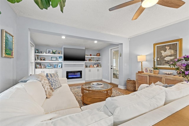 living area with a textured ceiling, a glass covered fireplace, wood finished floors, crown molding, and ceiling fan