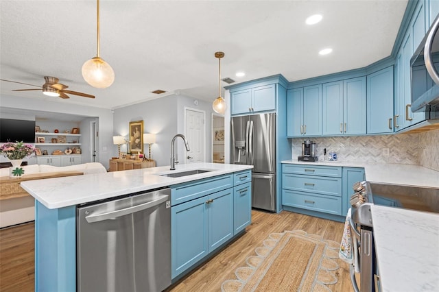 kitchen with blue cabinets, open floor plan, appliances with stainless steel finishes, and a sink