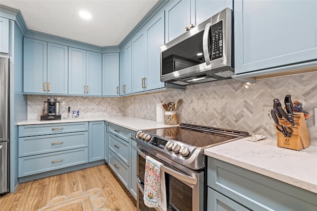 kitchen featuring light stone countertops, blue cabinetry, stainless steel appliances, decorative backsplash, and light wood-style floors