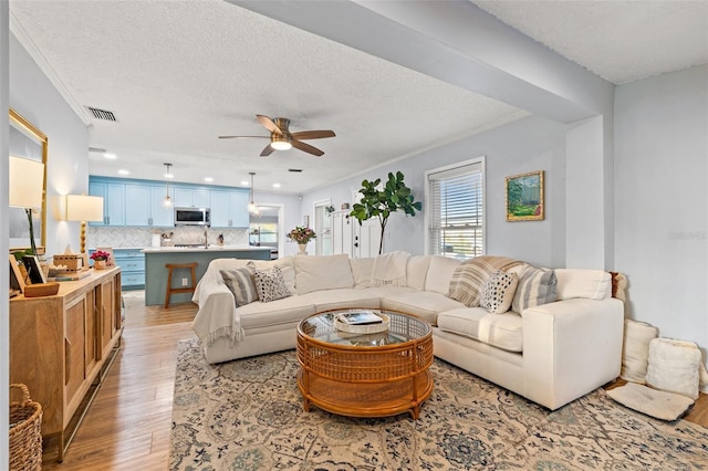 living room featuring a ceiling fan, visible vents, light wood-style flooring, a textured ceiling, and crown molding