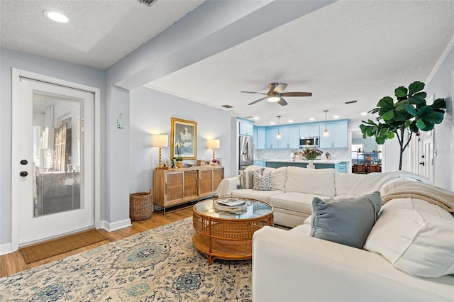 living room featuring baseboards, ceiling fan, ornamental molding, light wood-style flooring, and a textured ceiling