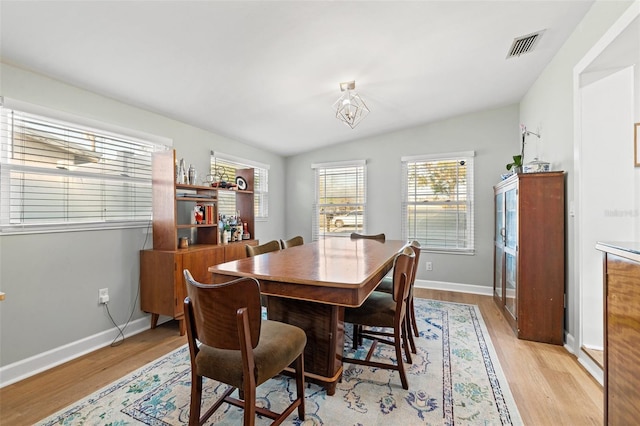 dining space with visible vents, baseboards, light wood-style floors, and vaulted ceiling