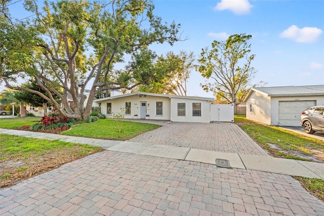 mid-century home featuring stucco siding, driveway, a front yard, and a gate