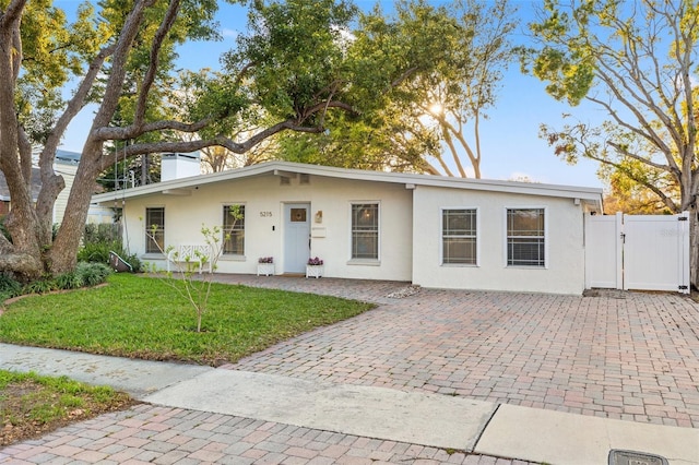 view of front of property with stucco siding, driveway, a front lawn, a gate, and fence