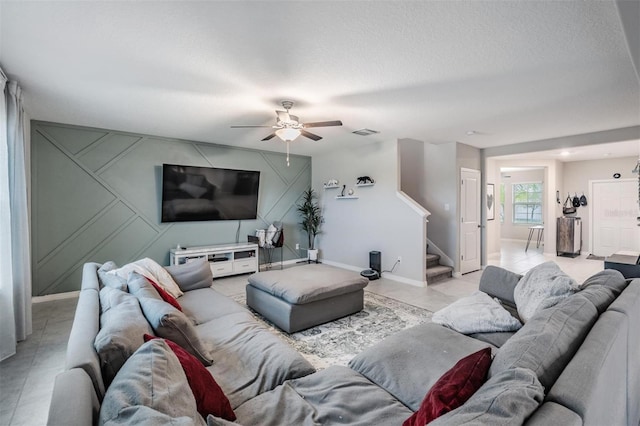 living room featuring a ceiling fan, baseboards, visible vents, stairs, and a textured ceiling