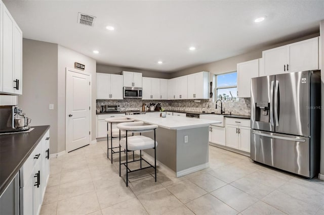 kitchen with visible vents, appliances with stainless steel finishes, white cabinetry, a kitchen breakfast bar, and backsplash