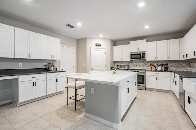 kitchen featuring visible vents, decorative backsplash, appliances with stainless steel finishes, white cabinetry, and a center island