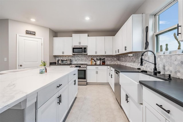 kitchen featuring light tile patterned floors, decorative backsplash, appliances with stainless steel finishes, white cabinetry, and a sink