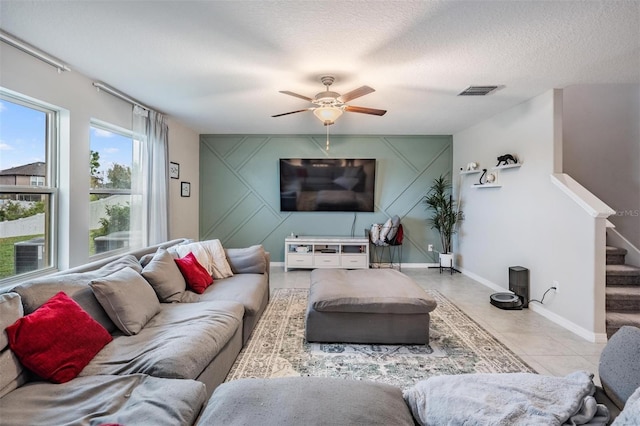 tiled living room with stairway, a ceiling fan, baseboards, visible vents, and a textured ceiling